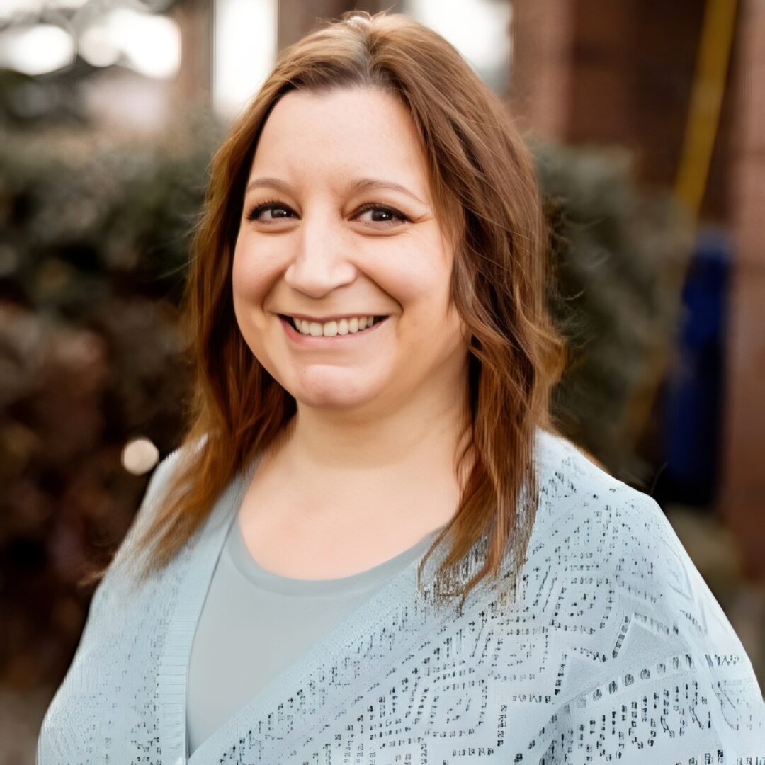 Smiling person outdoors wearing light blue sweater.